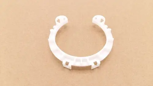 Weißer Kunststoffring mit Montageelementen, geeignet für Remeha Produkte. Der Ring hat eine offene Form und ist auf einem braunen Hintergrund abgebildet.